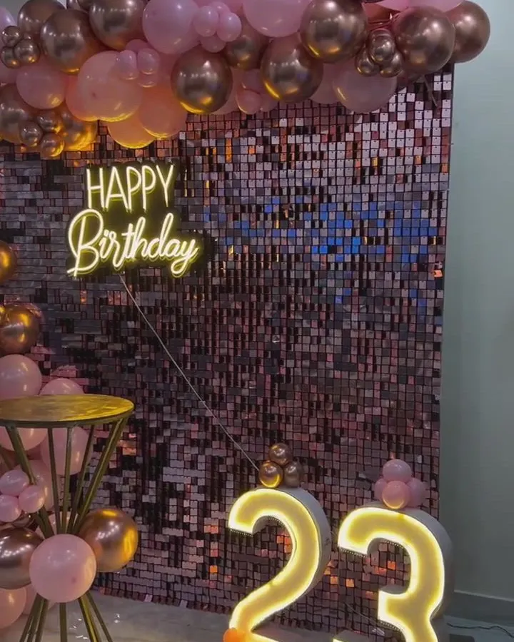 An elegant 23rd birthday setup combining a shimmering rose gold sequin wall with a custom neon sign and large marquee numbers. The organic balloon garland in rose gold and pink tones adds a sophisticated touch, perfect for milestone birthdays and anniversaries.