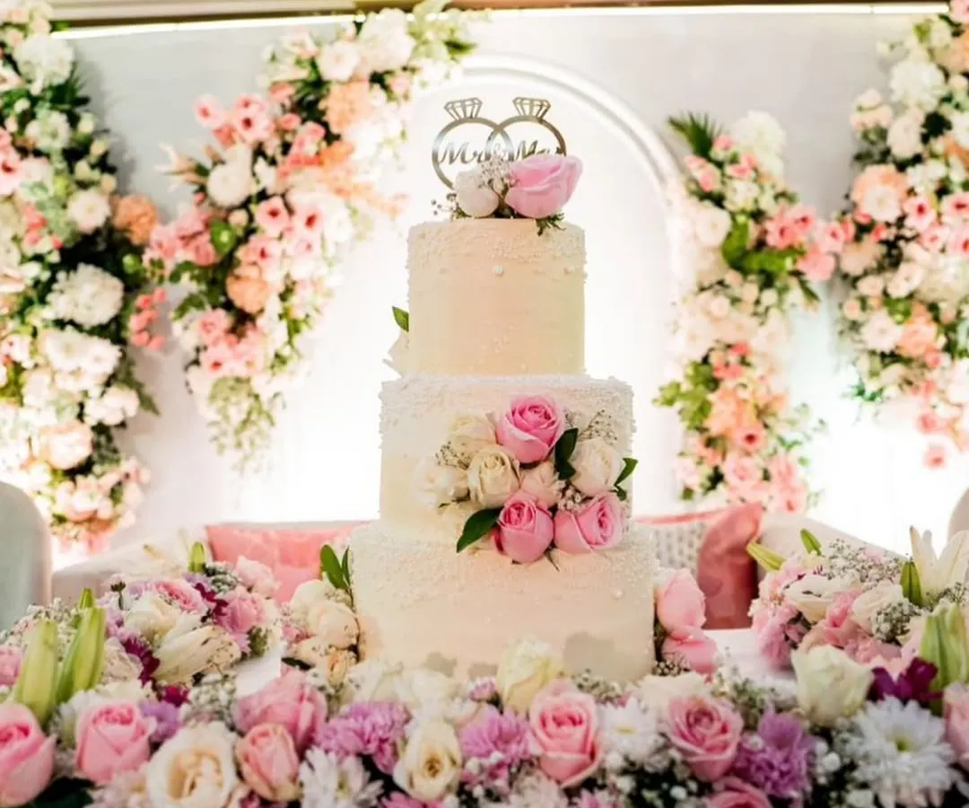 A wedding cake should be as magical as the love story it celebrates. This three-tiered buttercream cake, adorned with fresh pink and white roses and a custom "Mr & Mrs" topper, was the centerpiece of a beautiful floral-themed reception.