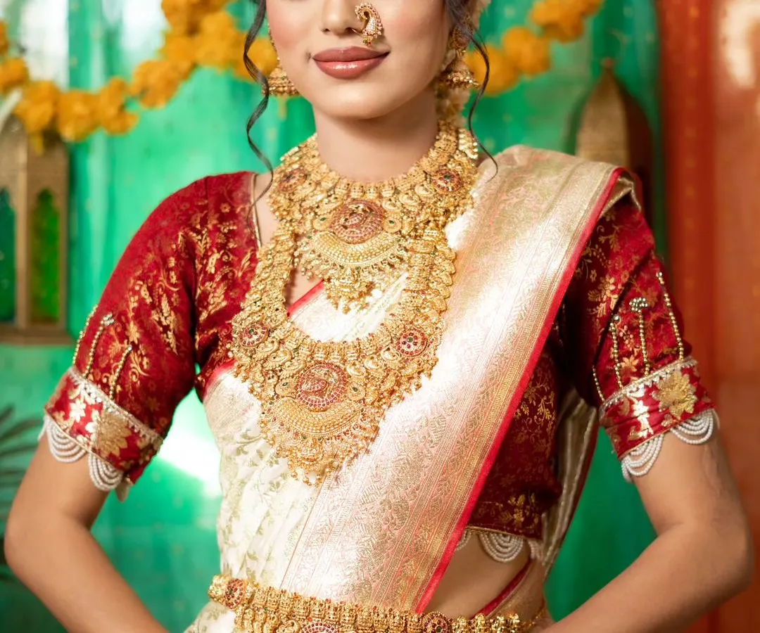 This is my classic South Indian temple jewellery set, featuring intricate gold work with goddess motifs. The set includes a choker, a long haram necklace, jhumkas, a maang tikka, and a kamarbandh, perfect for a traditional bridal look.