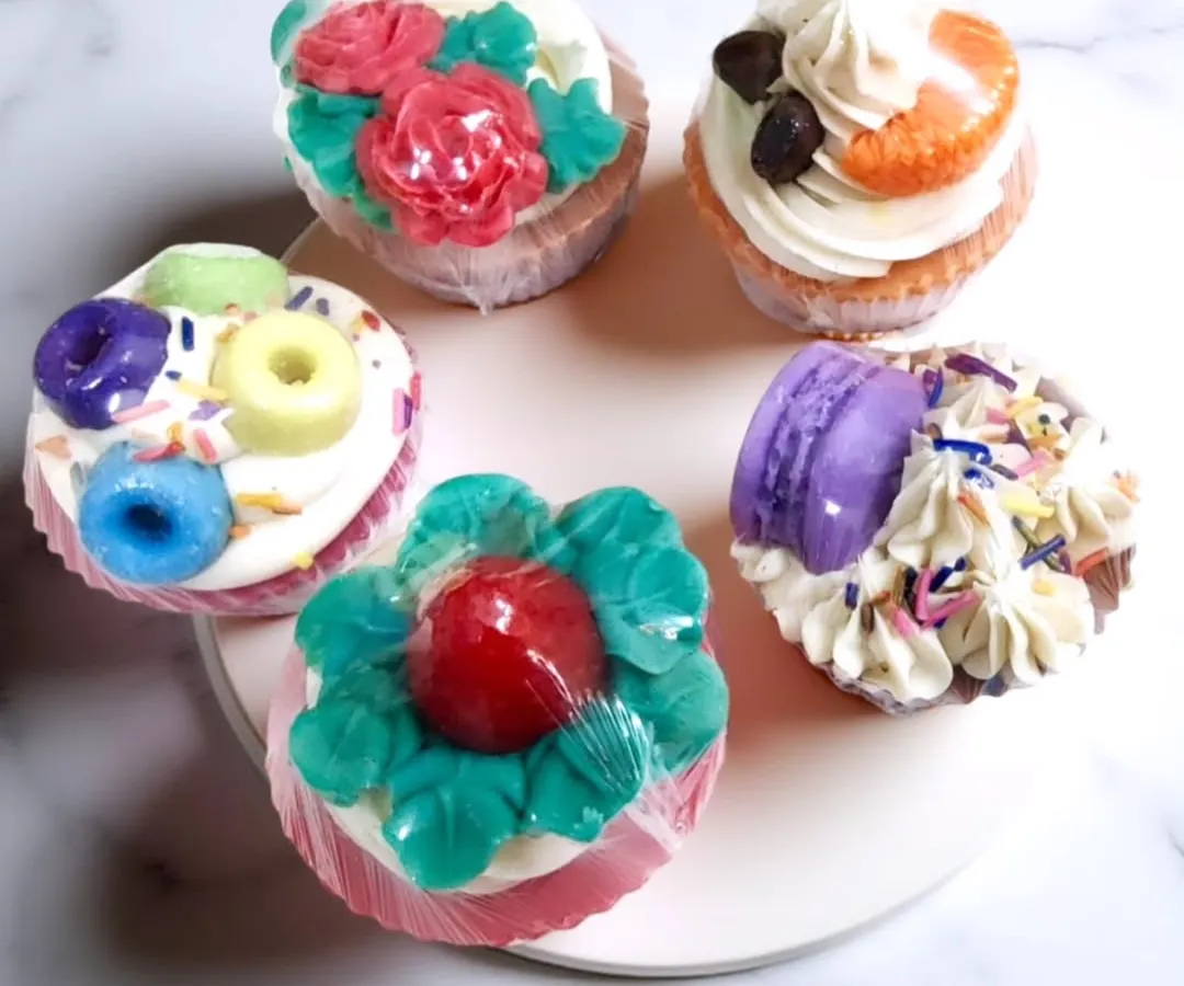 These are my cupcake soaps, and they are almost too cute to use. Each one is handcrafted with a piped frosting top and unique decorations like tiny macarons, roses, or coffee beans, making them a delightful and whimsical treat for your skin.