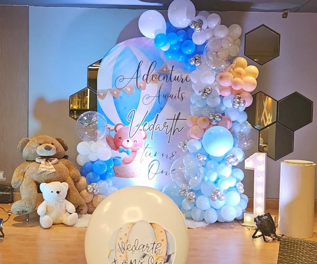 A full view of a vibrant 'Adventure Awaits' first birthday party. This hot air balloon and teddy bear theme shows our detailed work with custom backdrops, elaborate balloon garlands, and marquee lighting.