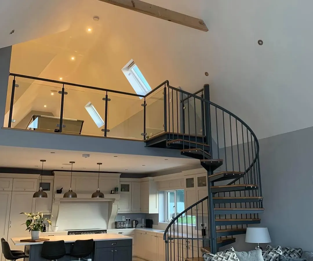 A bespoke spiral staircase connecting a living area to a mezzanine. It serves as a functional sculpture and a central feature of this beautiful open-plan home.