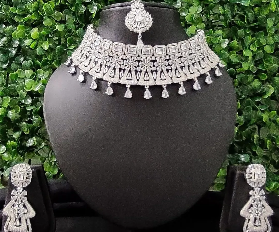 For the modern bride who loves to sparkle, this complete American diamond necklace set is a perfect choice for a reception or cocktail event. It includes a choker, matching earrings, and a delicate maang tikka.