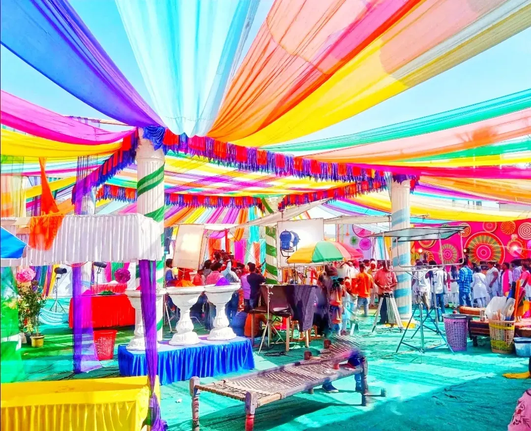 This is a large-scale Holi party pandal I decorated. I used vibrant, multi-colored fabric drapes across the ceiling and arranged traditional charpai seating to create a lively and authentic desi celebration space for the community.