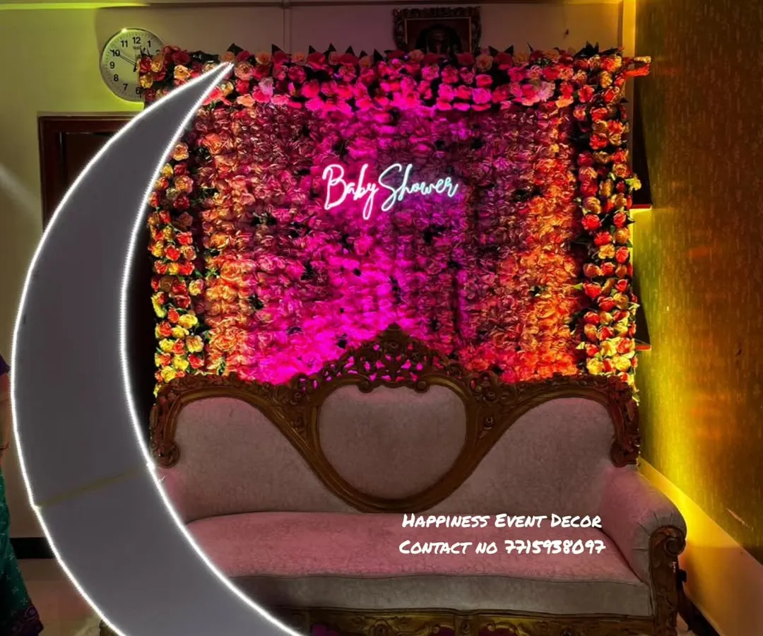For more intimate home functions, I can create beautiful backdrops like this one. This baby shower setup features a dense wall of artificial flowers, a custom 'Baby Shower' neon sign for a modern touch, and an elegant sofa, perfect for photos.