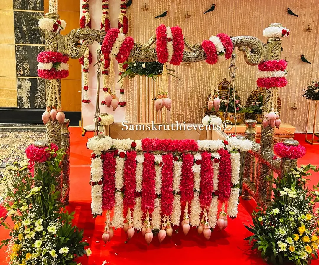 For a naming ceremony, the cradle is the star. Here, we've decorated a beautiful silver cradle with garlands of red and white flowers, accented with delicate lotus buds, making it a perfect centerpiece for welcoming the new baby.