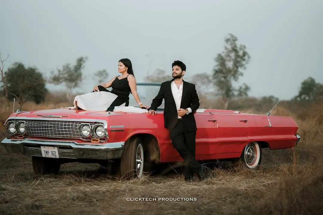 A stylish couple poses with a classic red convertible for their vintage-themed pre-wedding shoot in a rustic Goan landscape. This showcases how we can incorporate unique props to tell your story.