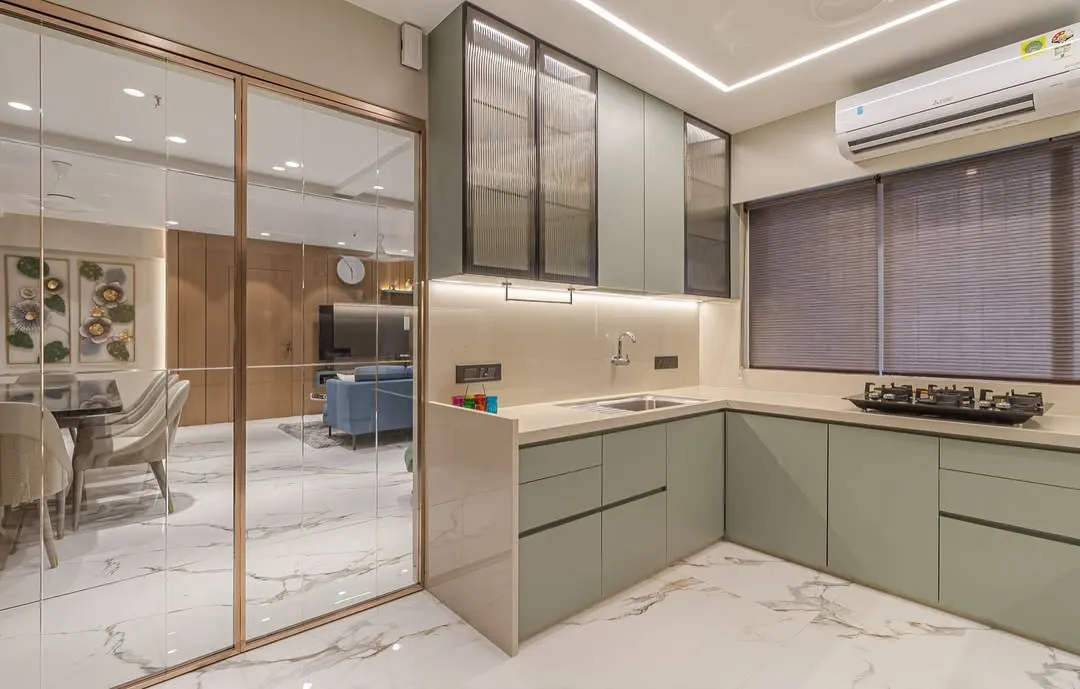 This modern kitchen features custom sage green cabinetry and a functional L-shaped layout. We used fluted glass on the upper cabinets and integrated lighting to create a bright, stylish, and highly practical workspace that opens into the main living area.