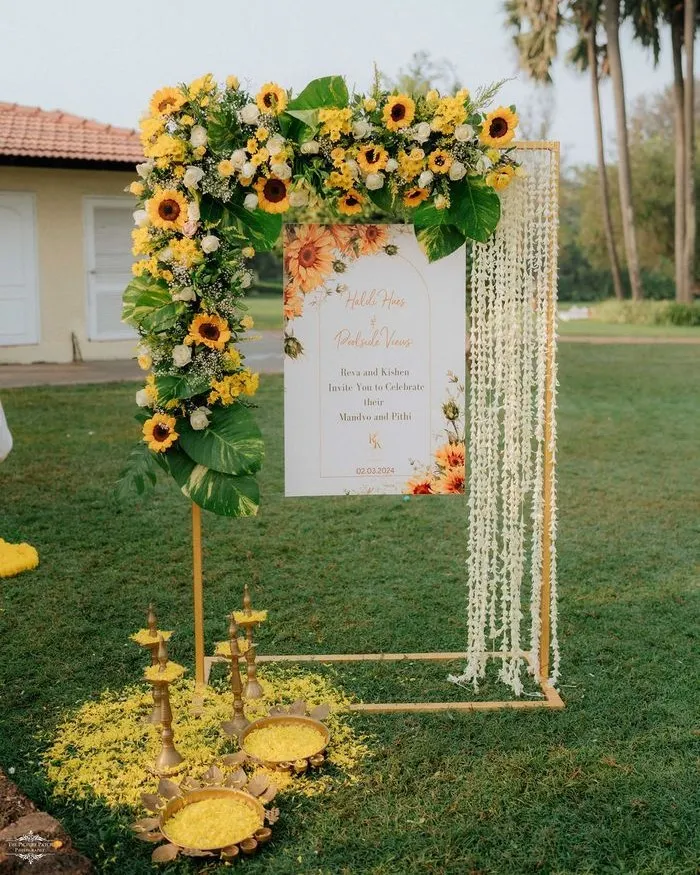 For this outdoor Haldi ceremony, we created a welcoming entrance that blends modern design with tradition. The custom sign is framed by an arc of fresh sunflowers and delicate jasmine strings, with brass lamps adding a customary touch.