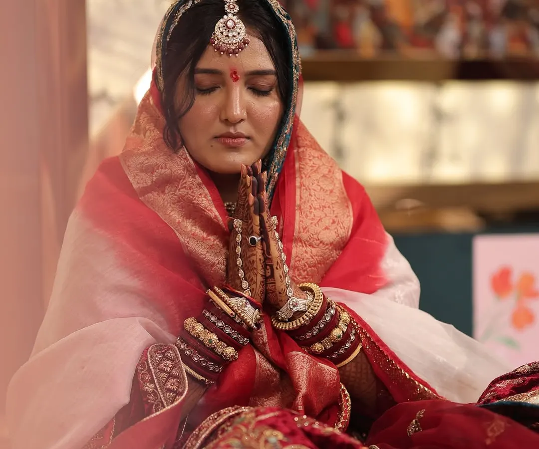 A serene moment captured for a traditional Marwadi bride. The makeup is subtle yet defined, with a focus on flawless skin, a classic red bindi, and defined eyes to complement the royal bridal attire and intricate jewelry.