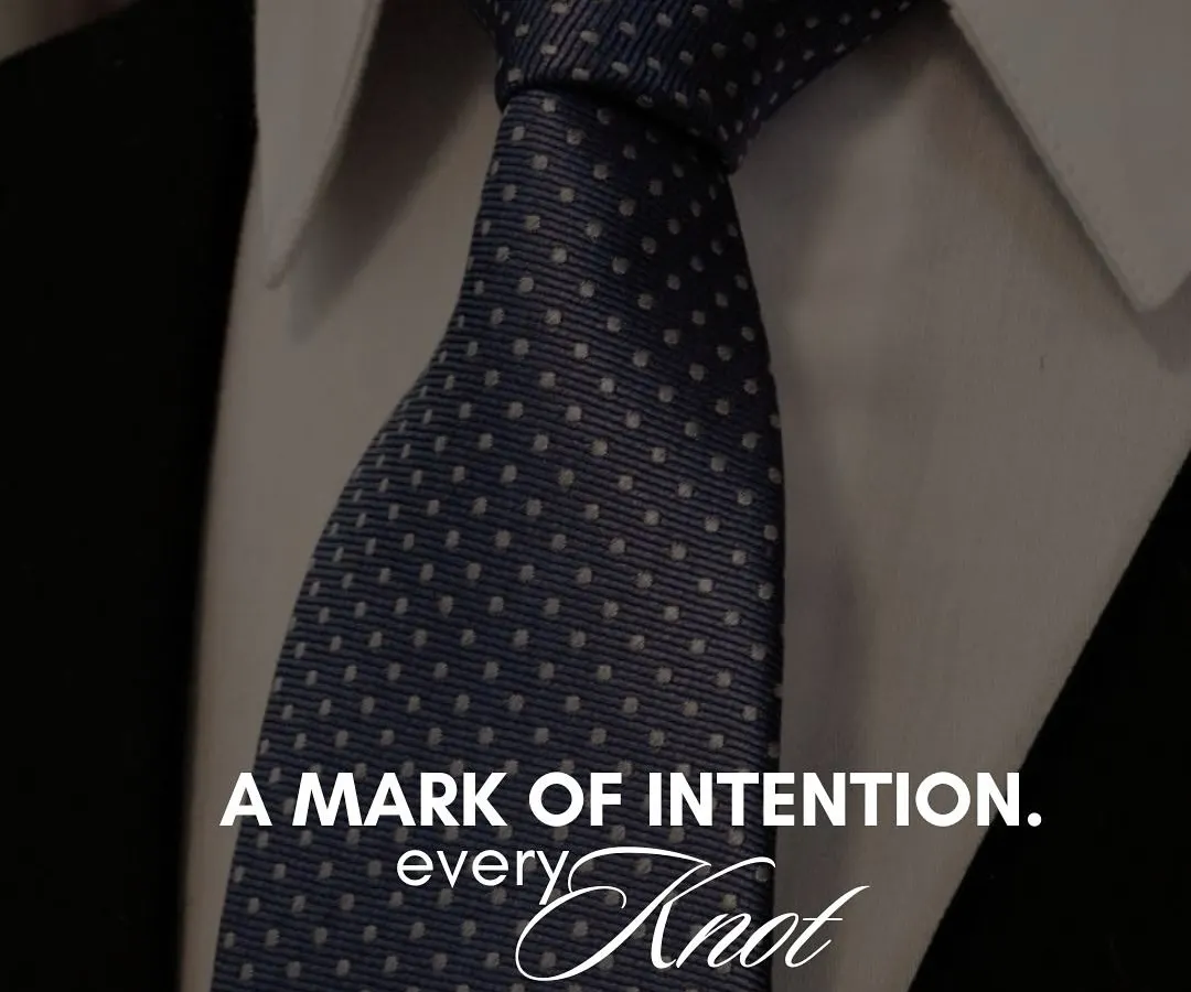 A tie is more than a formality; it is a mark of intention. This close-up of a perfectly knotted navy blue tie with subtle white polka dots illustrates our belief that every detail, no matter how small, contributes to the story your style tells.