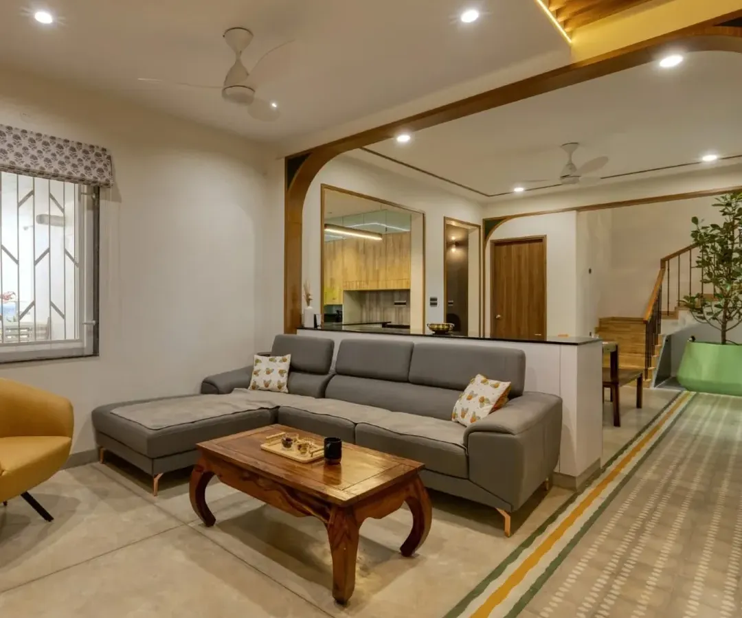 An open-plan living space designed for connection and calm. We crafted the custom grey sectional sofa and the solid wood coffee table to anchor the room, while wooden arches create a seamless flow into the dining area, embodying our warm minimalist approach.