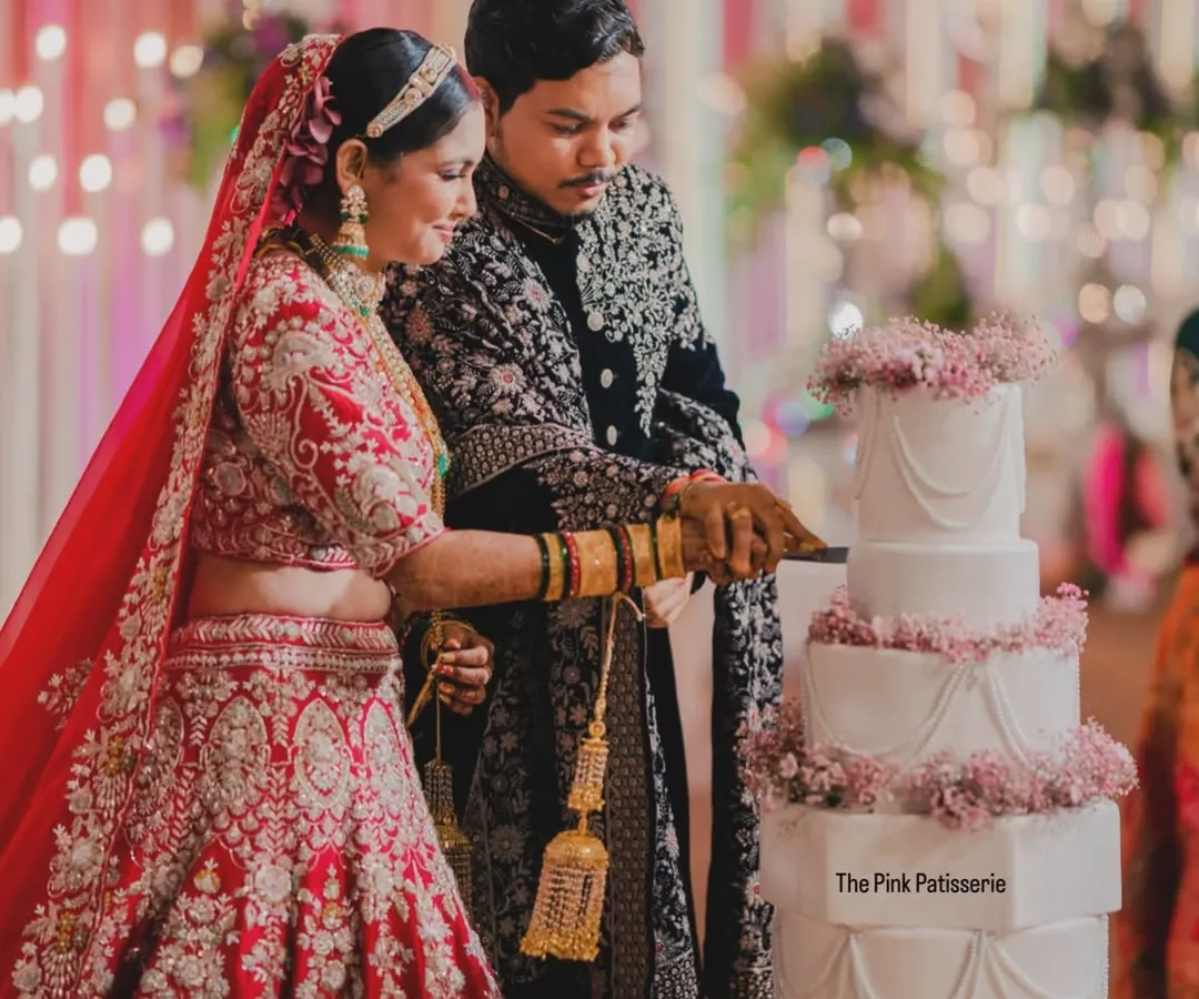A beautiful moment captured as the happy couple cuts into their five-tiered classic white wedding cake. The cake is elegantly decorated with swags of delicate pink flowers, making it a timeless choice for a grand wedding.