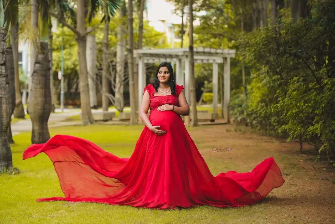 A stunning solo portrait of a mother-to-be in a vibrant red flowing gown, standing in a lush green park. This shot is all about celebrating the power and beauty of pregnancy.