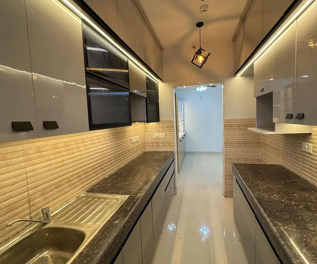 We designed this sleek parallel kitchen to be both beautiful and functional. It features high-gloss grey laminate cabinets, a durable granite countertop, and integrated under-cabinet LED lighting that makes the workspace bright and inviting.