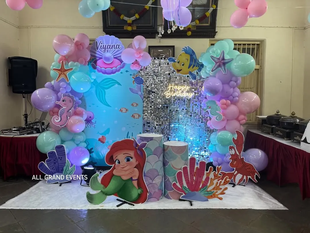 For kids' parties, I bring their favorite stories to life. This 'Under the Sea' birthday party features a complete setup with a Little Mermaid theme, including character cutouts, a shimmer backdrop, themed props, and a custom balloon arrangement in pastel colors.