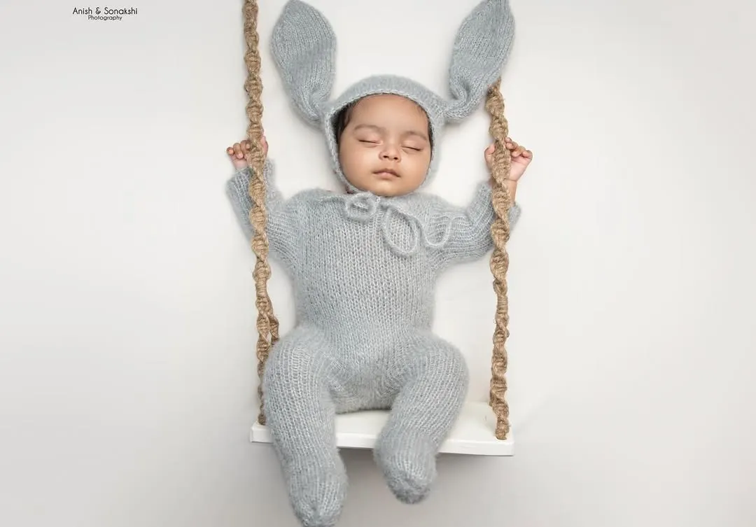 Our "posed and dreamy" sessions are all about creating adorable, artistic portraits. This little one is sleeping so peacefully in our popular hand-knitted bunny costume, perched on a custom-made swing prop. It's a perfect example of the gentle, styled newborn photography we love to create.