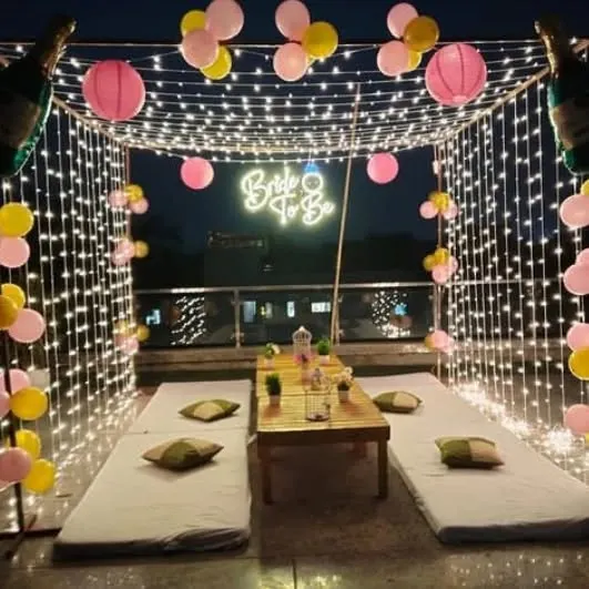 For a trendy and modern celebration, I can arrange a rooftop cabana like this one for a 'Bride to Be' party. The setup includes a canopy of fairy lights, comfortable low seating, a custom neon sign, and balloons to create a magical atmosphere.