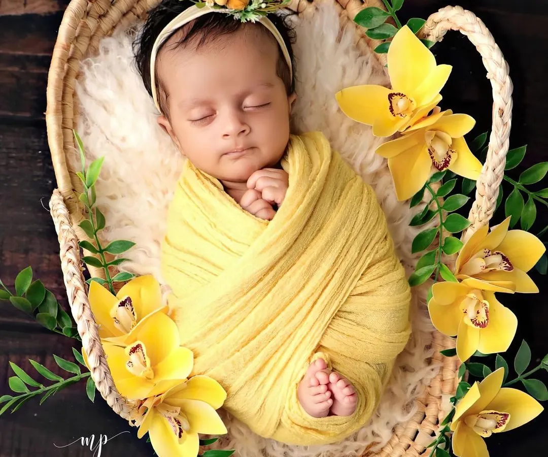 The definition of peaceful slumber. This newborn is swaddled snugly in a vibrant yellow wrap, nestled in a rustic basket and surrounded by beautiful matching flowers, showcasing our classic posed photography style.
