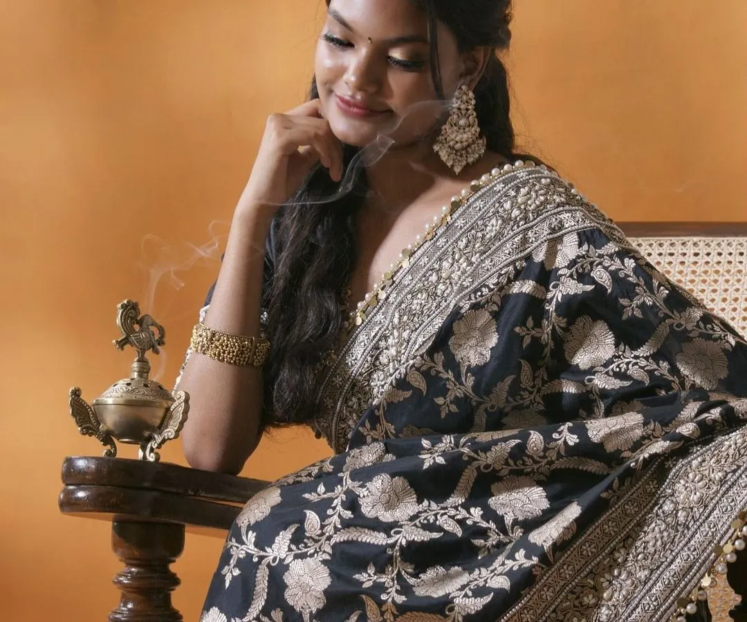 This portrait captures a moment of quiet reflection, blending traditional elegance with a contemporary mood. The intricate details of the black and gold saree are highlighted by soft, directional lighting, creating an image that is both artistic and deeply personal.