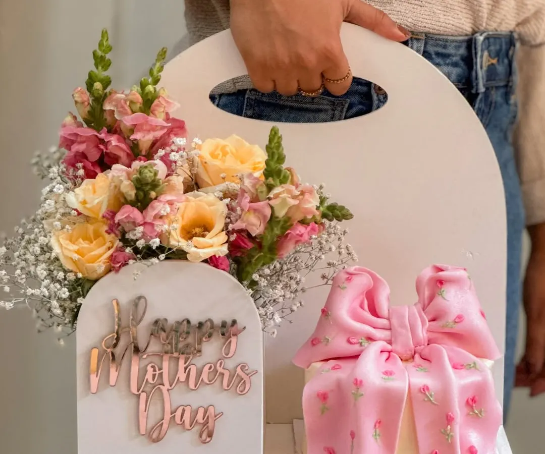 The 'Bloom Box' collaboration, a unique gift set featuring a delicate cake with an intricate pink bow alongside a fresh floral arrangement in a custom white carrier. This design showcases how I blend edible art with fresh flowers for a truly special Mother's Day gift.