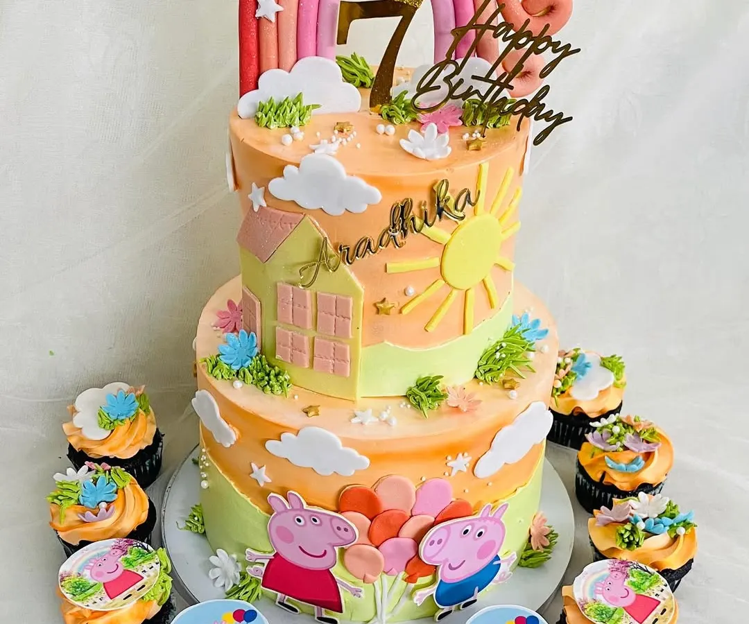 A cheerful two-tier Peppa Pig cake, perfect for a sunny 7th birthday. This design features a warm sunset color palette, a rainbow topper, and adorable edible prints of Peppa and George, complete with matching themed cupcakes.