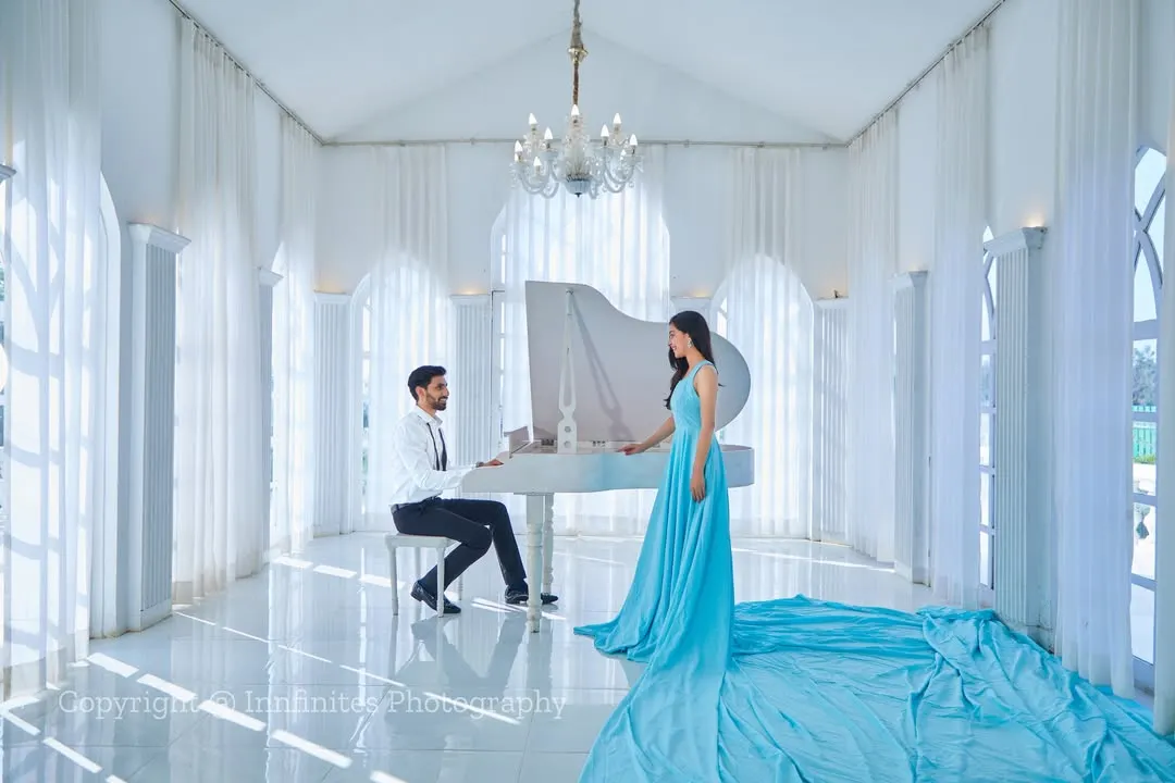 Our all-white studio, complete with a grand piano, provides a backdrop for timeless elegance. The flowing trail of this light blue gown adds a touch of drama and sophistication to this classic couple portrait.