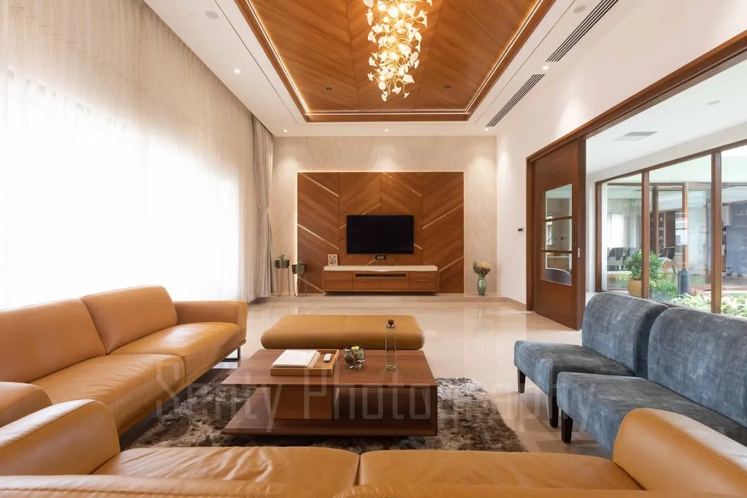 This expansive living area in one of our farmhouse projects showcases our approach to warm, luxurious interiors. We use a palette of rich textures, including natural wood ceilings and polished marble floors, to create a space that is both grand and inviting, with abundant natural light.
