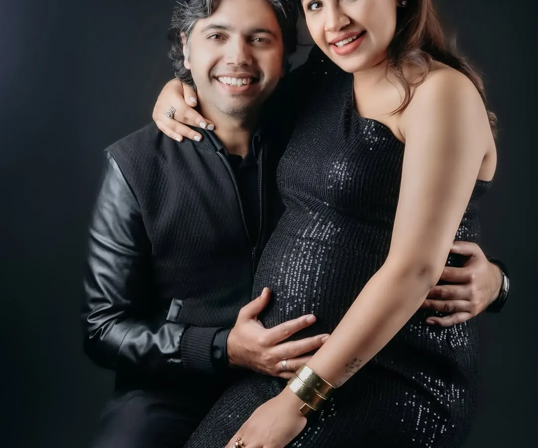 A glamorous studio portrait of an expecting couple. The mom-to-be shines in a black sequin dress while her partner holds her close, creating a timeless and elegant memory.
