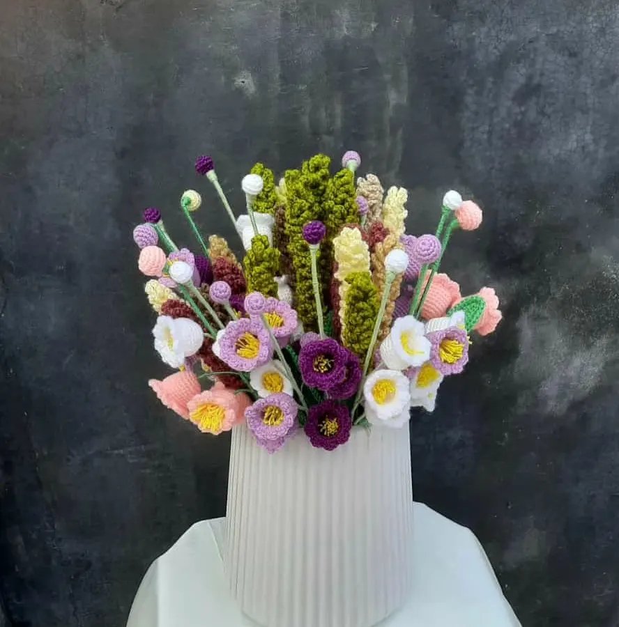 A full, vibrant bouquet of my crochet wildflowers arranged in a modern white vase. This piece includes a mix of purple, white, and yellow flowers with varied textures and green foliage, showing how my work can be a lasting centerpiece.