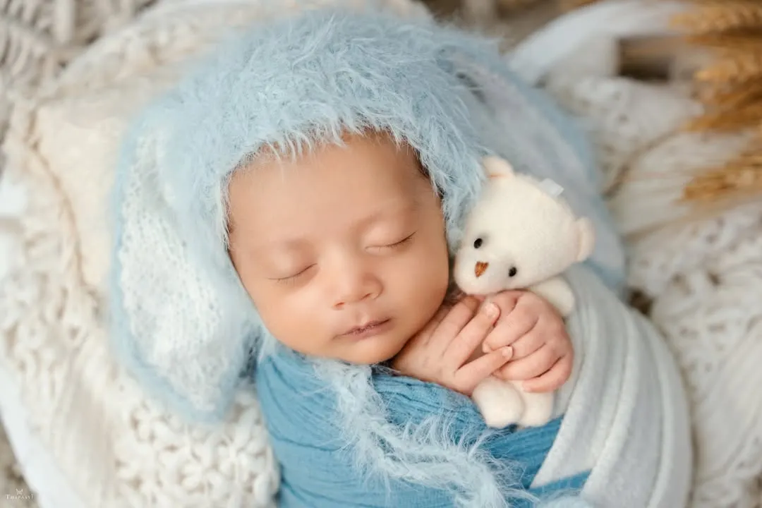 The peaceful, fleeting moments of a newborn are my specialty. I focus on safe and comfortable posing, using soft wraps and textures to create a serene portrait, like this little one dreaming sweetly with his tiny teddy bear.