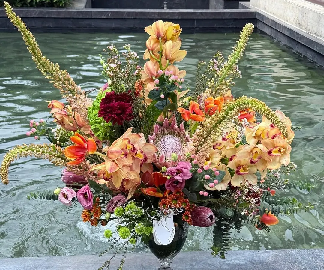 An arrangement that sings of saffron and tangerine. I brought together exotic protea, vibrant eremurus, and delicate orchids to create a piece full of texture and warm energy, perfect as a striking centerpiece for your home.