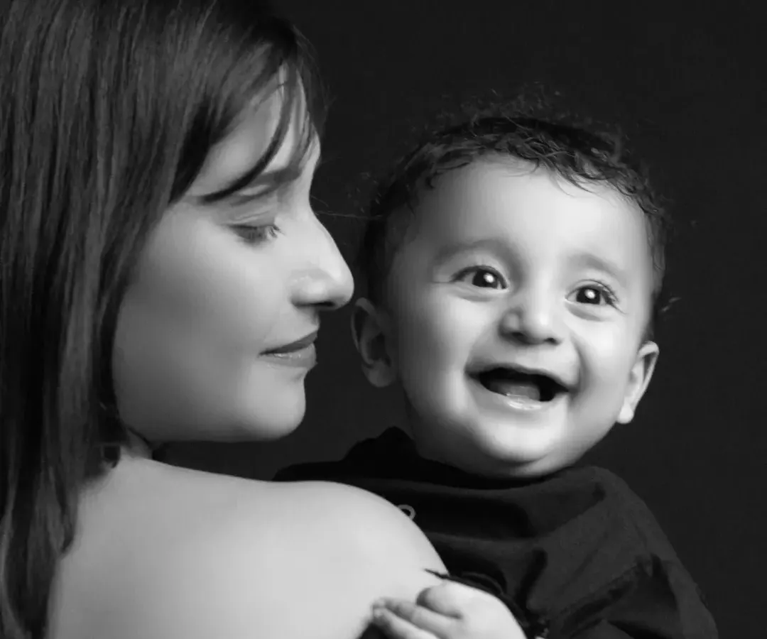 There is nothing more pure than a child's laughter. In this classic black and white studio portrait, the focus is entirely on the joyful connection between mother and baby. The dramatic lighting isolates their expressions, creating a powerful and timeless memory of a fleeting moment.