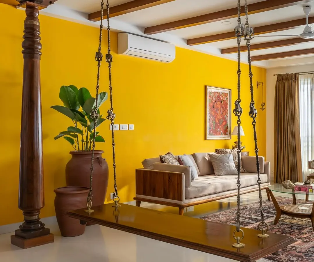 In our 'Vasudhalayah' project, we created a warm, ethnic living room centered around a traditional wooden swing and antique Chettinad pillars. The vibrant yellow accent wall and custom teak furniture create an inviting space for family gatherings.