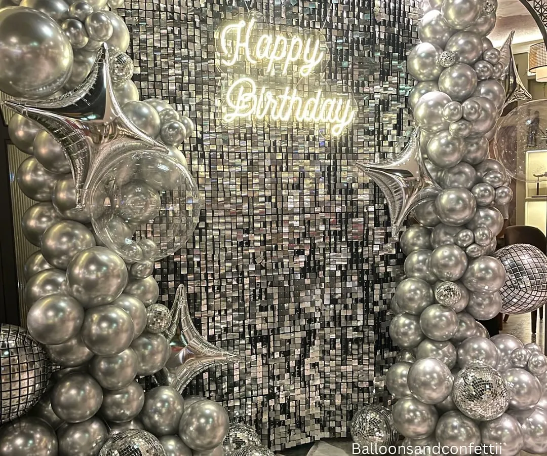 For a birthday that needs to be extra, I designed this full glam setup. It features a silver shimmer wall that catches the light perfectly, framed by an organic arch of chrome and silver balloons, disco balls, and a custom "Happy Birthday" neon sign. This is how you make a statement.