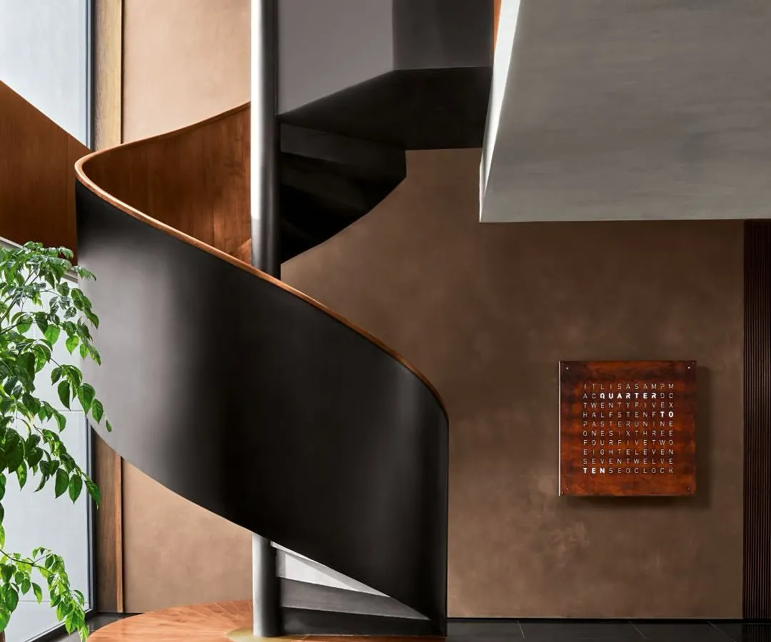 This sculptural spiral staircase, crafted from matte black metal and polished wood, serves as an architectural anchor in the Urban Hearth residence. Its form is designed to create a sense of quiet ascent, turning a functional element into a piece of art.
