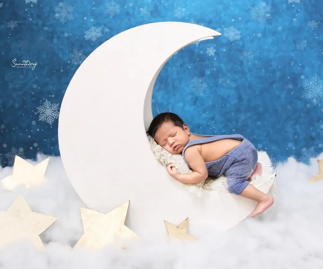 For a touch of magic, I love creating dreamy scenes like this one. Here, a peacefully sleeping baby rests on a crescent moon prop, surrounded by soft clouds and stars. Your baby's safety is always my priority during these creative newborn poses.