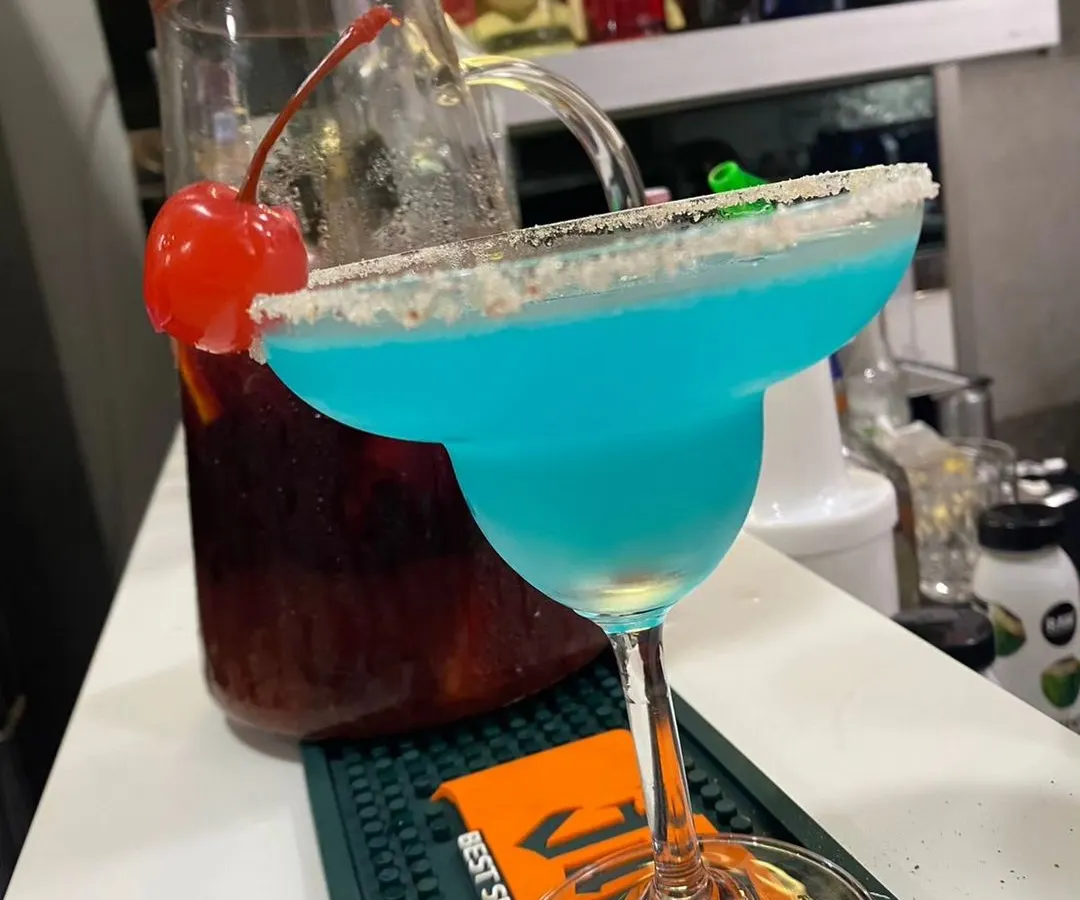 A vibrant Blue Lagoon cocktail, expertly crafted and ready to be served. We pride ourselves on creating visually stunning drinks using premium spirits and fresh ingredients, like this one with a classic sugar-rimmed margarita glass and cherry garnish.
