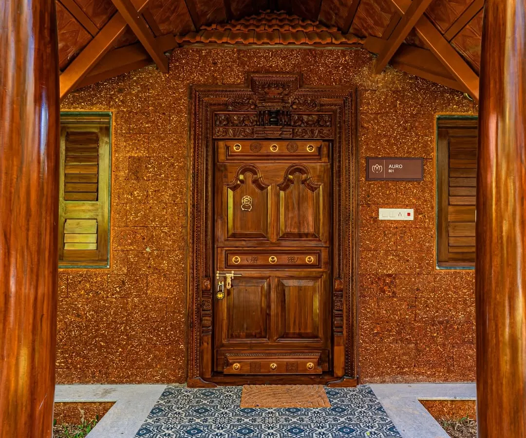 Detail is everything in architecture. This intricately carved wooden door, set against a rustic laterite brick wall and framed by traditional pillars, creates a grand and welcoming entrance for a resort project. It's a nod to timeless Indian craftsmanship.