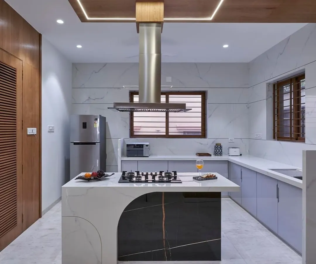 We designed this modern kitchen around a stunning marble island with an integrated cooktop, making it the true heart of the home. The combination of sleek, light-grey cabinetry, a stainless steel chimney, and warm wood accents creates a perfect balance of function and style.