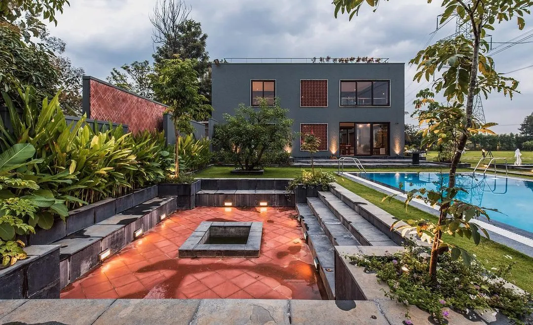 This is our award-winning project, 'The Grey Grotto', a contemporary farmhouse on the outskirts of Bengaluru. The design seamlessly integrates the home with its landscape, featuring a sunken lounge, a swimming pool, and expansive green spaces for true indoor-outdoor living.