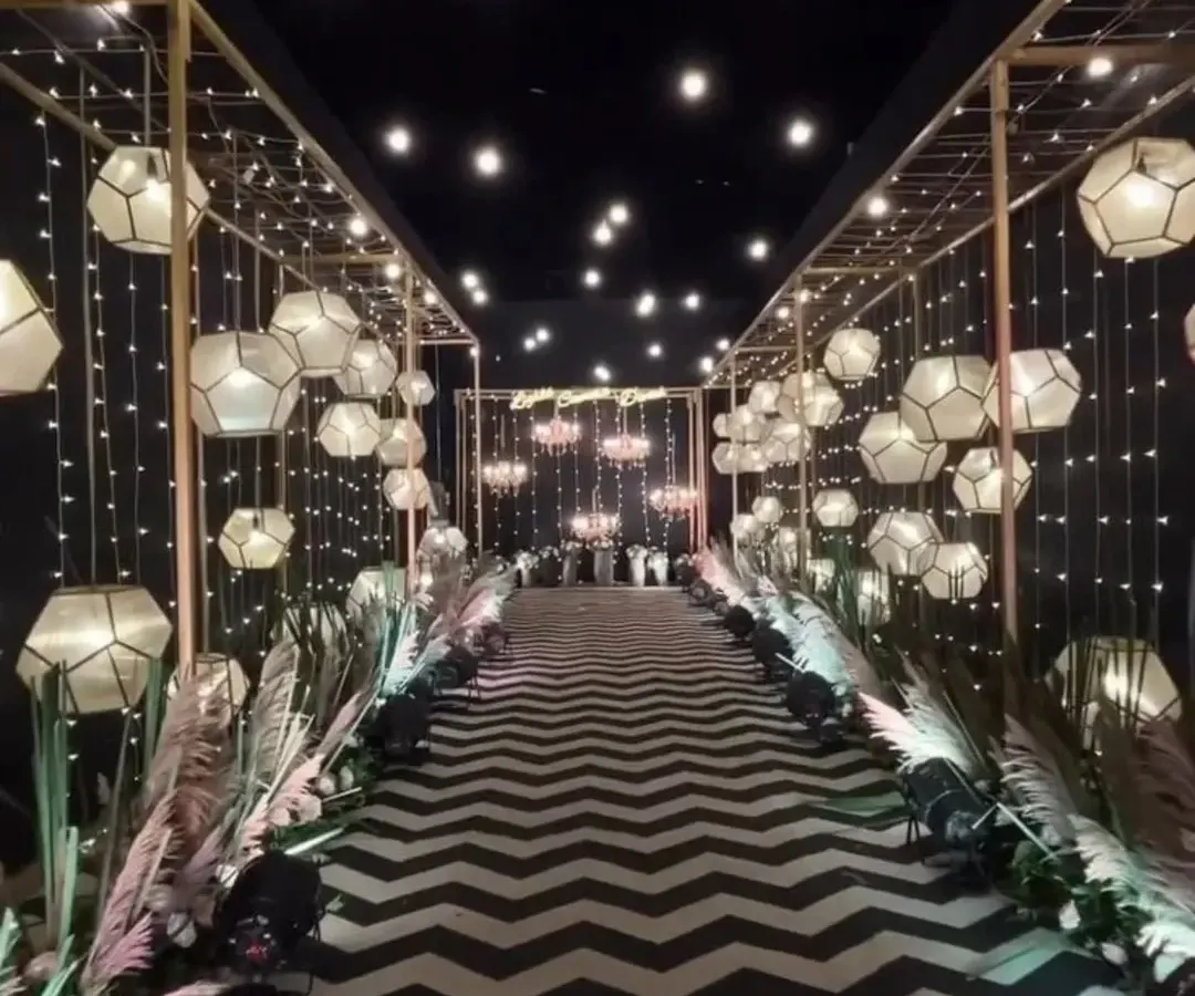For a truly dramatic and modern entrance, I can design something unique like this. The combination of a black and white chevron carpet, geometric lanterns, and warm fairy lights creates an unforgettable walkway for your guests.