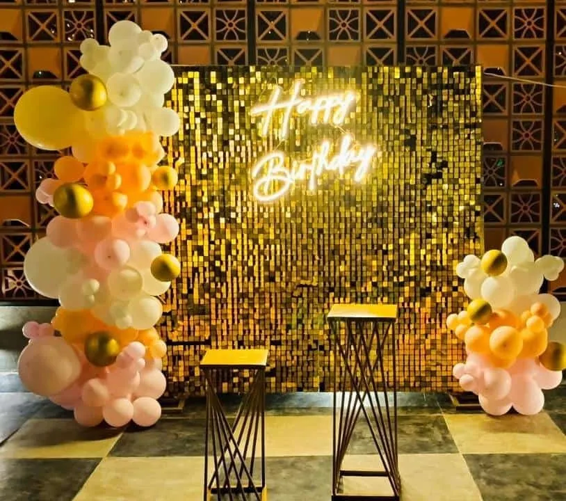 A popular choice for birthdays and parties, this photo booth combines a shimmering gold sequin wall with a custom "Happy Birthday" neon sign. The organic balloon garland in pastel and gold tones adds a modern, celebratory feel.