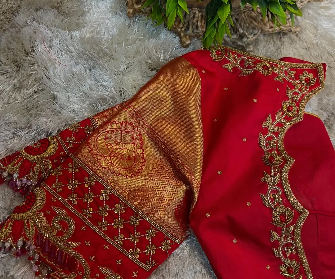 This is the kind of craftsmanship you will learn to create. This vibrant red bridal blouse features intricate gold Aari work along the neckline and sleeves, combined with traditional brocade fabric for a timeless look.
