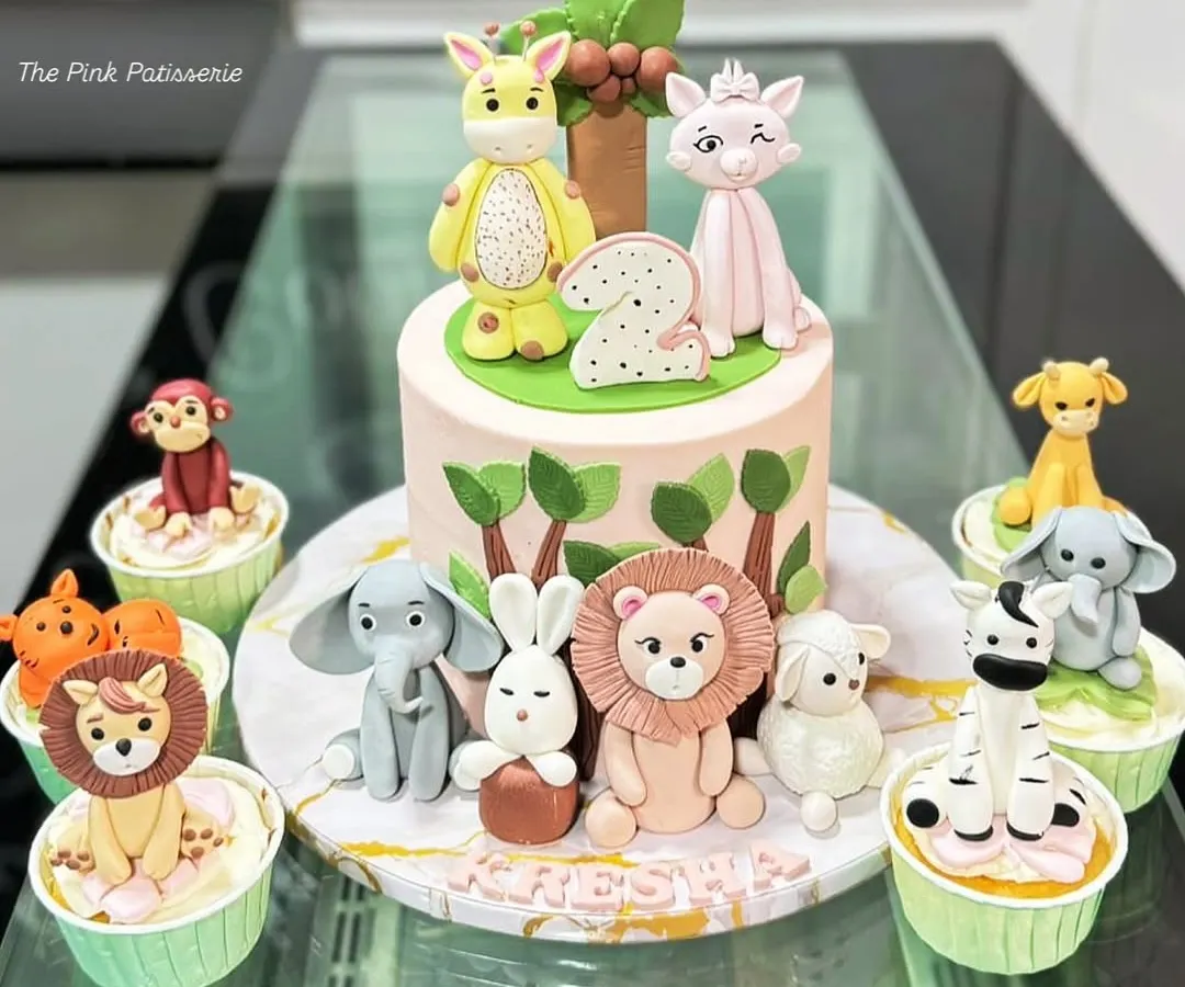 A complete party set for a jungle-themed second birthday. This includes a central cake with adorable, handcrafted fondant animals and a matching set of cupcakes, each topped with a different creature like a lion, elephant, and zebra.