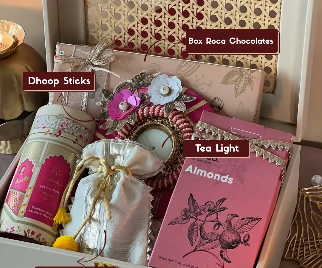 This is my classic 'Gulabi Noor' Diwali hamper, beautifully arranged in a reusable rattan box. It shows exactly what you get, from aromatic dhoop sticks and a decorative tea light to delicious Roca chocolates and chikki-filled potlis.