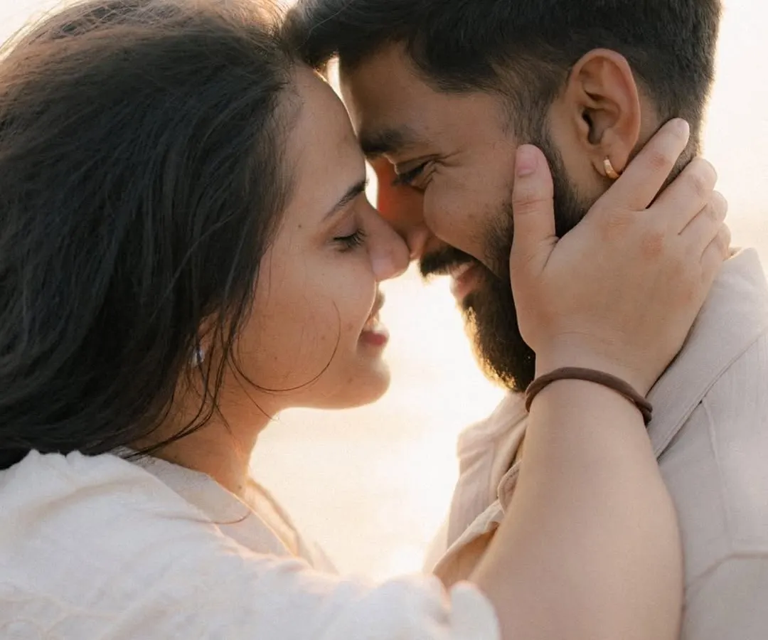 An intimate close-up of a couple on the beach at sunset. They are touching foreheads and smiling, bathed in the warm, golden light, capturing a moment of pure connection and love during their golden hour couple photography session.