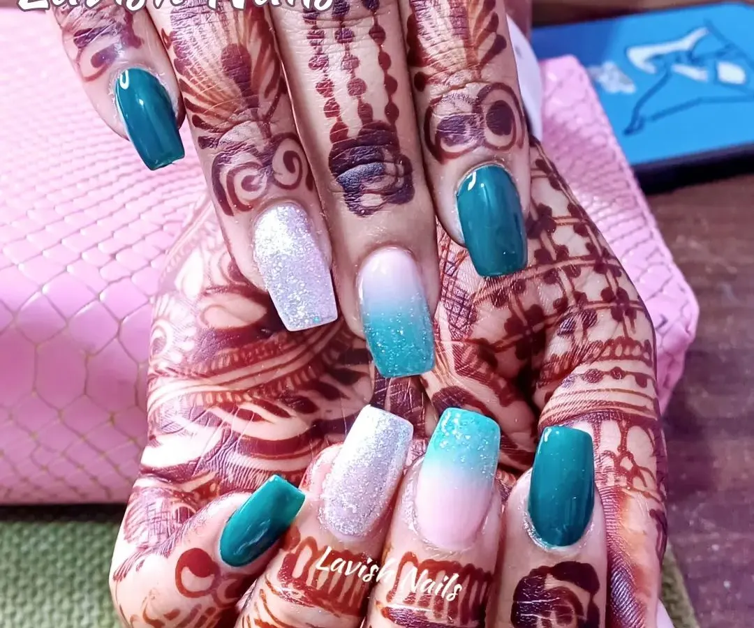 This design shows how beautifully colored nails can complement bridal mehendi. The set combines solid teal, white glitter, and a soft teal-to-nude ombré for a vibrant, photo-ready look.