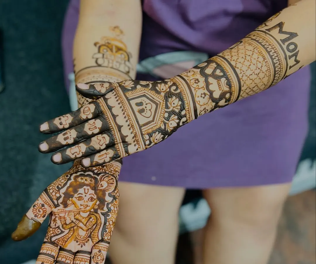 I love creating personalized mehendi for baby showers. This design features a portrait of baby Krishna on one palm and the word "MOM" on the forearm, celebrating the journey into motherhood with unique and meaningful art.
