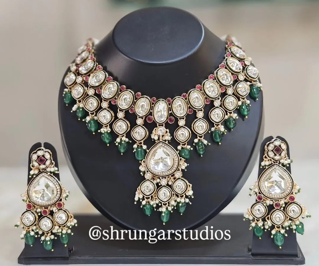 A classic and elegant Kundan bridal set that never goes out of style. This necklace and earring set features large, uncut polki-style stones, beautifully contrasted with deep green and ruby-red beads. It's a versatile choice that complements a wide range of bridal lehengas and sarees.